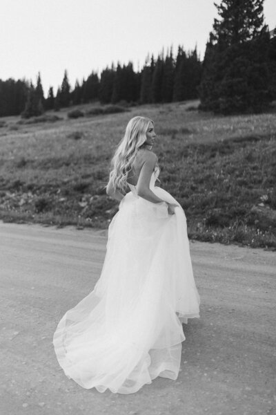 bride holding up her wedding dress while standing on a dirt road