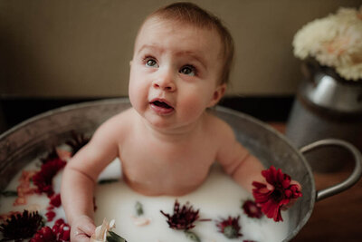 Baby sitting in a milk bath with red flowers