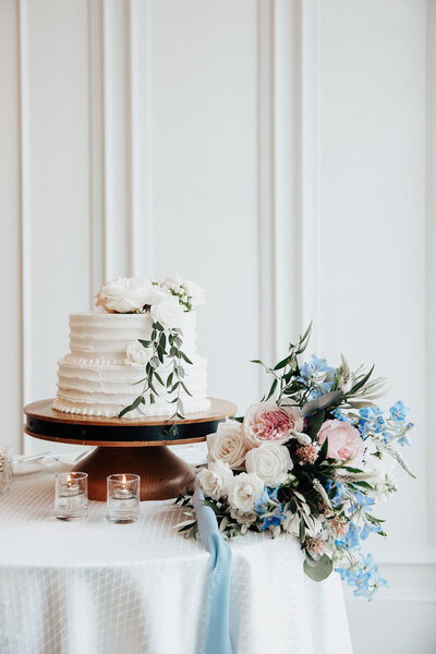 Elegant creme wedding cake with bouquet on table. Blue ribbon and flowers.