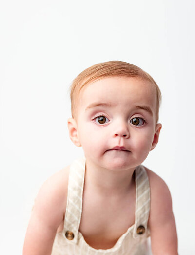 A cute baby stares into the camera during his One Year Photo Session in a white studio.