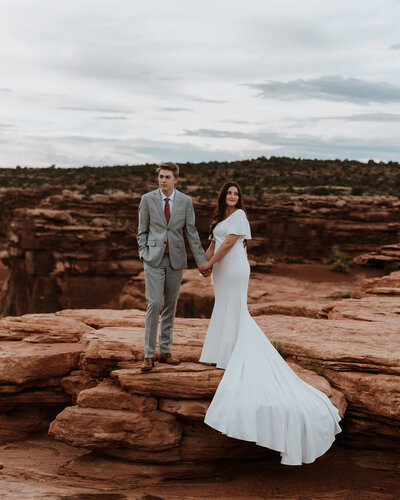 bride and groom standing on red rock