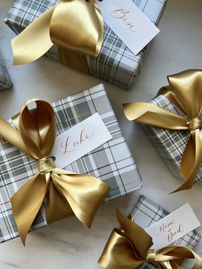 White gift tags with gold calligraphy on presents with plaid wrapping paper