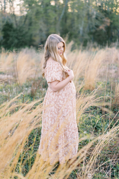 Pregnant woman in free people dress in a field of tall grass by Richmond family photography education Adrianne Shelton
