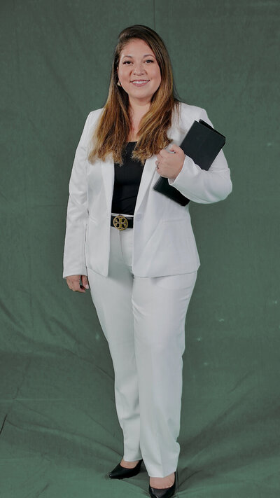 Teresa Cordoba stands in a white pantsuit while holding a book.