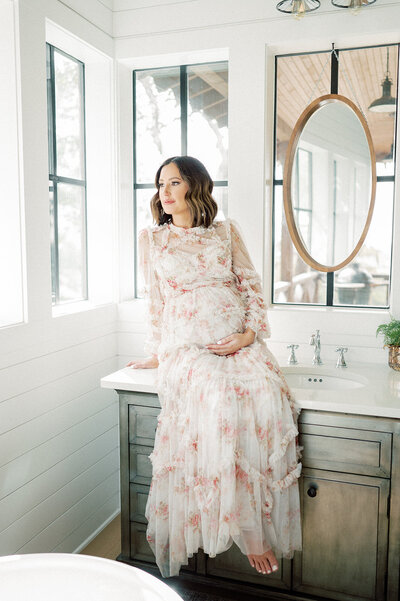 a mother sits on the counter in her bathroom holding her pregnant belly