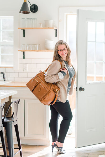 Amanda Richardson, North Carolina brand photographer, walks out the front door carrying her camera bag and suitcase behind her