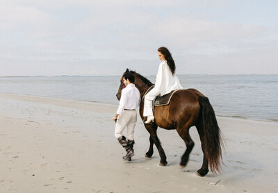 Bride and groom walking with a brown horse in natural setting