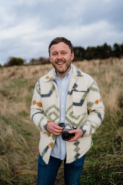 Aberdeen wedding photographer Scott Arlow  sits on a wall outside in the Aberdeenshire countryside.