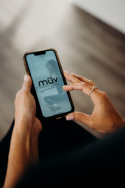 A close-up of a woman's hands, holding an iPhone, while opening an exercise app that was created exclusively for MUV Chiropractic in Boulder, Colorado.