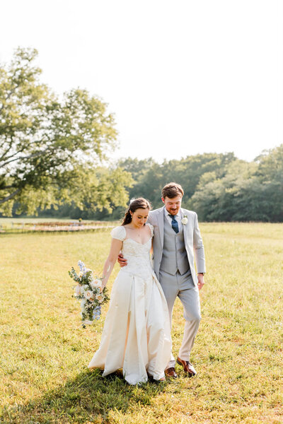 ride and groom walking hand-in-hand through a sunlit field, the bride holding her bouquet and both smiling joyfully