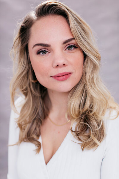 Castingfoto van zangeres Bernice Havenaar. Blond golvend haar, witte top en lichtgrijze achtergrond.