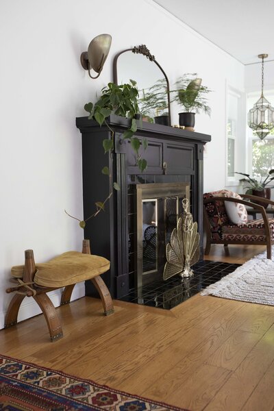 Black fireplace with plants and mirror on the mantel representing interior design by Winsome Home Interiors.