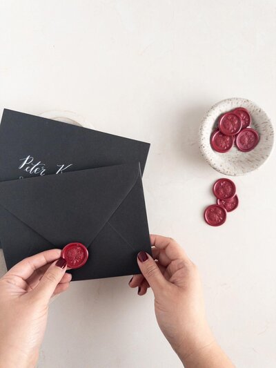 DC Calligrapher assembling custom wedding invitations, attaching a red wax seal on a black envelope