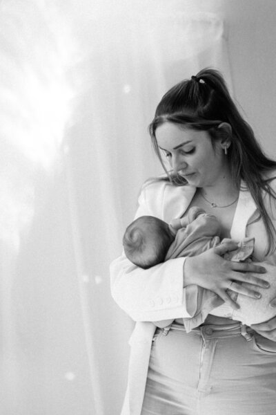Een vrouw houdt een baby in een draagdoek, met een liefdevolle blik en een rustige omgeving op de achtergrond.