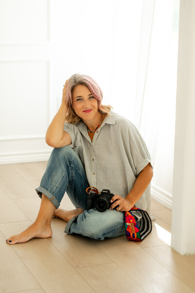 Emily, owner and family photographer of Poppy + Blue Photography in Fort Worth, Texas, sitting with her camera in natural light studio
