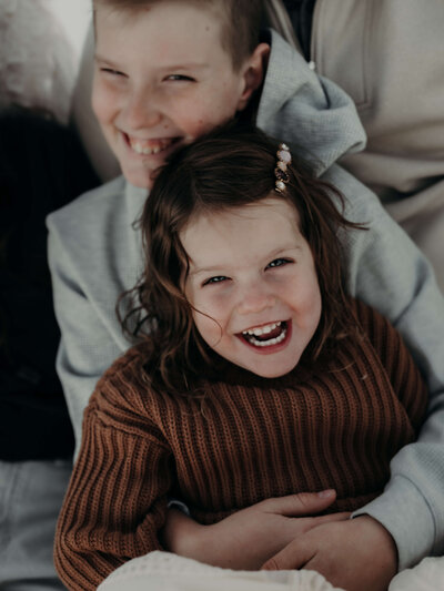 A big brother grins as he holds his little sister in a hug during an outdoor photo session.