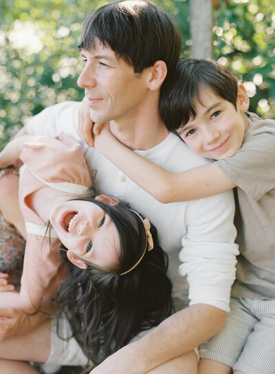 dad with two young kids smiling and hanging n him