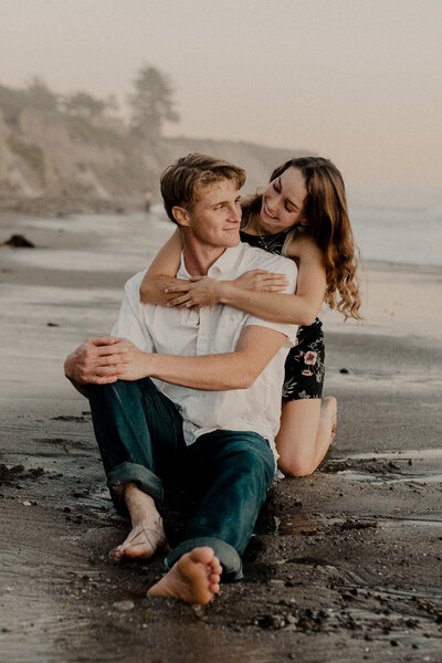 a couple taking their engagement pictures at shell beach sitting in the water with playful photography