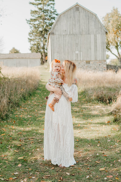 Mommy gently kissing her baby near a beautiful barn.
