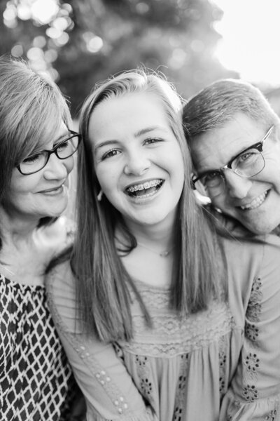 Black and white image of teenager girl laughing with mom looking at her sweetly and dad laughing to her other side.