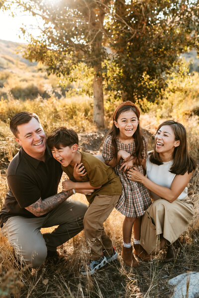 Mother and father squatting down and tickling their two young kids at sunset in Mayberry Park Verdi.
