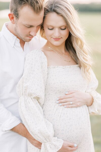 Maternity photos done at sunset outdoors in a field while holding bump and looking at bump