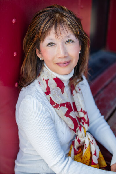 Headshot photography of an Asian woman with white shirt and scarf posing by a red caboose in San Juan Capistrano, CA