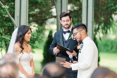 A groom reads his vows to the bride as she smiles. 