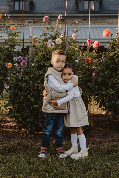 Two small children hugging in front of flowers 