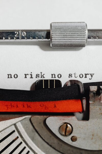 A close-up of a manual typewriter with a red ribbon that says in lowercase letters, "no risk no story."