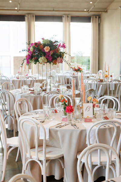 Modern indoor wedding reception with white chairs, pastel florals, and tall centerpieces, styled by a Wimberley wedding planning expert.