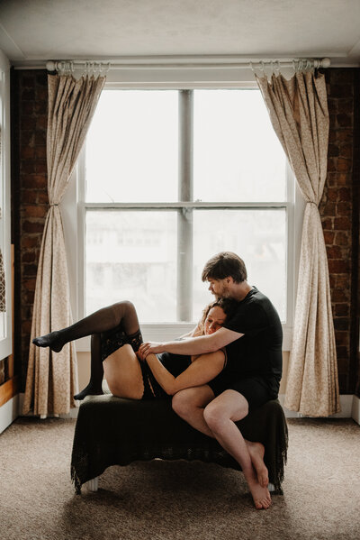 couple boudoir in front of window and brick wall in bloomington normal