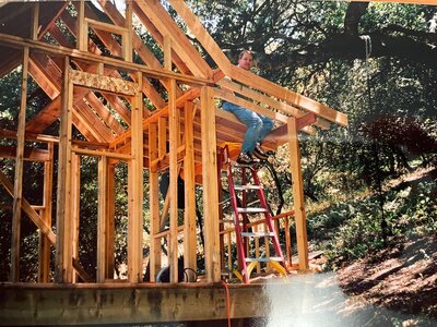 A contractor standing on a ladder while framing a wooden structure during an early-stage construction project.
