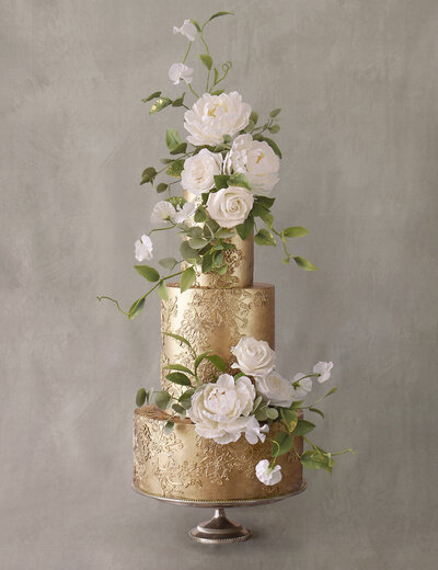 elegant gold wedding cake with white and cream sugar flowers, green foliage and subtle textured lace