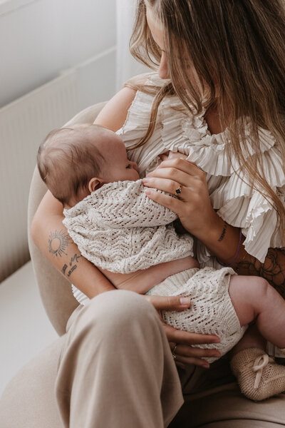 Newbornshoot thuis moeder houdt haar baby dicht tegen zich aan in zacht daglicht in Zeeland omgeving Goes. 