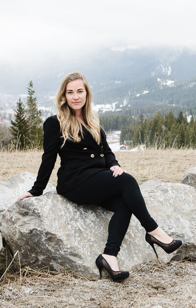 Realtor Tamara Rzan sitting against the picturesque pine trees and mountains of Pincher Creek