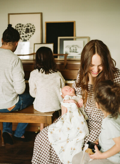 dad and daughter play piano while mom holds newborn and laughs with young son