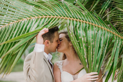 bride and groom kissing under a palm leaf