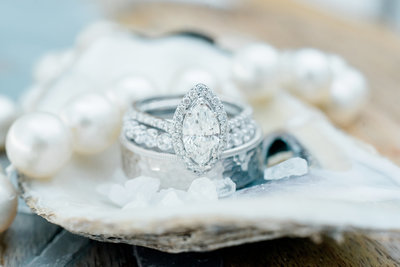 Stunning wedding ring sits in a shell next to strand of pearls