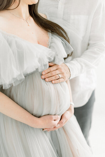 A close up maternity photo of a mother holding her belly  while her spouse is also embracing her belly while they are standing in a Dallas photography studio.