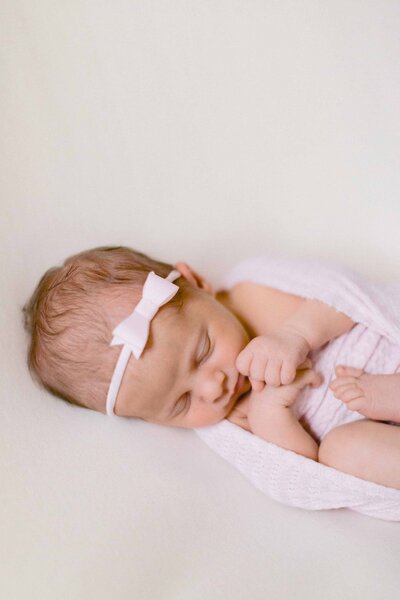 newborn baby girl snuggled in a pink swaddle with a pink bow on her head