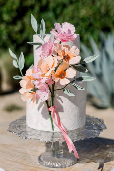2 tier white wedding cake with white floral stencil and peach and pink sugar flower bouquet