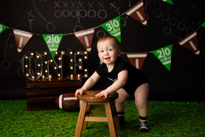 Toddler leaning on stool in front of football themed backdrop