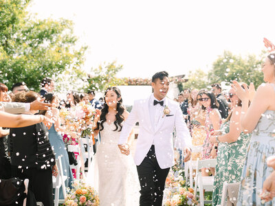 bride and groom exiting ceremony space at serendipity garden with confetti in their faces and excited laughter and joy