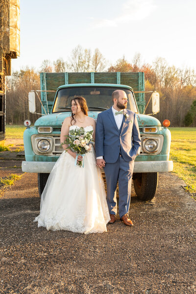 A wedding couple taking golden hour photos in front of  vintage blue farm truck.