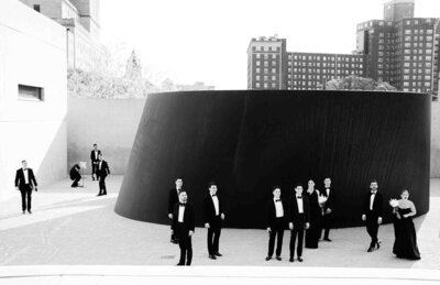 black and white photo of groomsmen in tuxedos  standing in front of a large urban sculpture