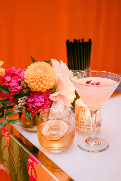 pink and yellow flowers on a table next to soft pink alcoholic drink in a martini glass