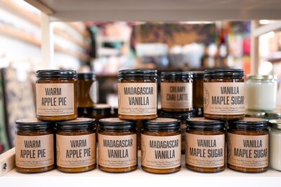 Beautifully styled product photo featuring artisanal candles displayed in a local gift shop. The image highlights the candle's packaging, textures, and warm ambiance, capturing the cozy and inviting atmosphere of the shop