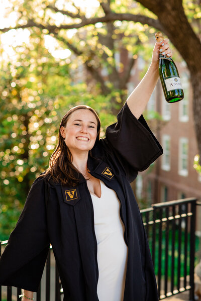 Senior holding a champagne bottle up while wearing graduation gown