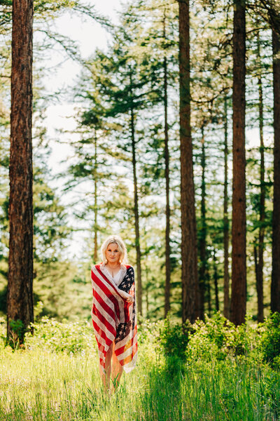 Woman in lingerie covered with American flag standing in Pattee Canyon forest